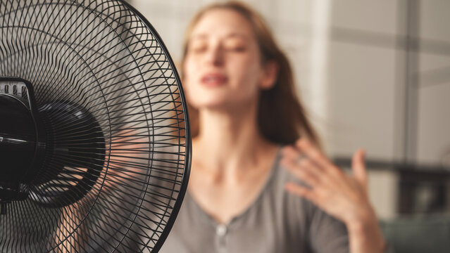 Woman cooling down by ventilator at home
