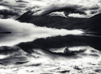 Dramatic black and white landscape of misty clouds rolling over a calm body of water, reflecting the sky