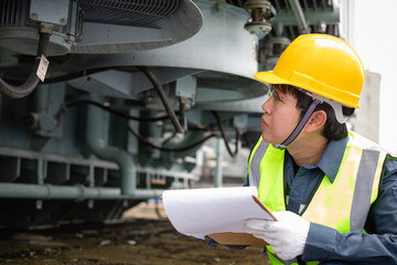 Worker wearing yellow helmet performs inspection of cooling system in transformer at substation...