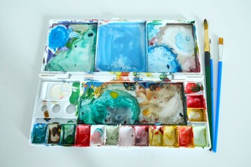 watercolor paints set, a used paint palette with brushes placed beside it