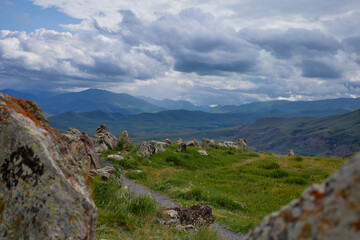 Scenic view of lush green hills and dramatic red cliffs under a bright blue sky with white clouds, showcasing the beauty of untouched mountainous nature and diverse rocky terrain.