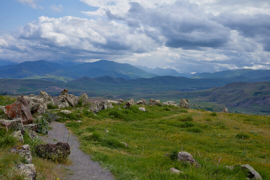 Scenic view of lush green hills and dramatic red cliffs under a bright blue sky with white clouds, showcasing the beauty of untouched mountainous nature and diverse rocky terrain.