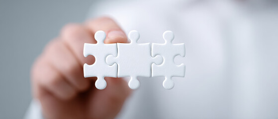 Hand holding three white puzzle pieces teamwork connection solution business concept closeup focus