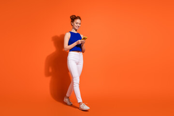 Young Woman in Casual Outfit Using Smartphone Against Vibrant Orange Background in Studio