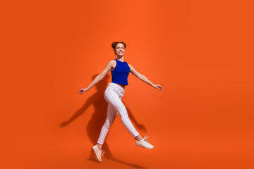 Active and joyful young woman in a vibrant outfit posing against an orange background, showcasing her cheerful mood