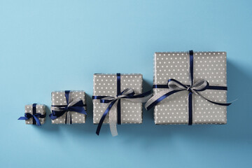Four gift boxes of different sizes are lined up on a pastel blue background. Each gift is decorated...