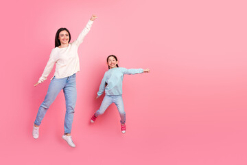 Mother and daughter joyfully jumping on a vibrant pink background, wearing casual attire,...