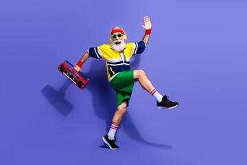 Energetic elderly man in retro sportswear holding boombox and striking a dynamic pose against a vibrant purple background