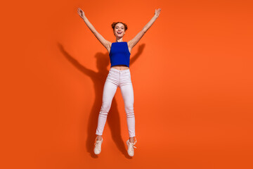 Energetic young woman in casual fashion jumping against a vibrant orange background, expressing joy and positivity