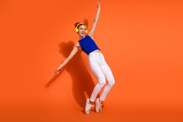 Young energetic woman dancing and smiling with headphones against a vibrant orange background, showcasing fun