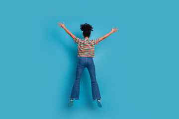 Young woman in stylish casual outfit with vibrant striped t-shirt and jeans standing against a teal...
