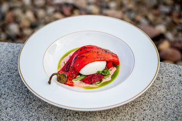 Freshly prepared burrata cheese sits atop grilled pepper slices, evoking summer's essence outdoors