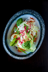 A vibrant fennel salad with fresh greens, herbs, and pink accents against a dark backdrop