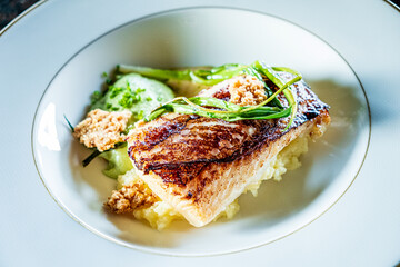 A beautifully presented grilled fish fillet on creamy mashed potatoes, accented with fresh greens