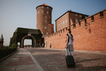 Tourist walking near wawel castle in krakow, poland, with rolling suitcase