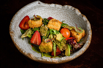 A colorful salad features crispy vegetable bites, fresh strawberries, and greens dressed with herbs