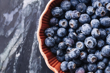 Fresh blueberries in ceramic bowl. Organic forest berries on marble table. Natural healthy fruit snack. Tasty summer harvest full of vitamins. Close-up of ripe seasonal blue berries.