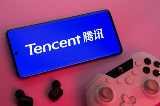 Dhaka, Bangladesh- 12 June 2025: Smartphone with Tencent logo, game controller, and earbuds on a pink background.