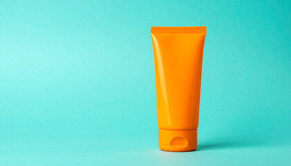 Blank orange cream tube. Cosmetic product. Beauty and skincare concept. Turquoise background.