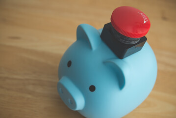 Red stop emergency button on blue piggy bank with wooden table background. Home finance or personal financial problem, economy crisis, savings not enough for payment, bankrupt and so on concept.