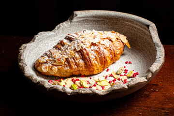 A delicious almond croissant on a textured plate, surrounded by colorful toppings, invites all