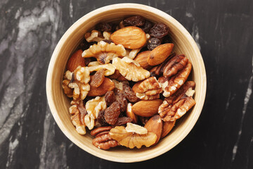 Mixed nuts in wooden bowl. Walnuts almonds pecans and raisins. Natural healthy snack full of energy. Close-up on marble table. Rustic style. Ideal for diet plans and clean eating habits.