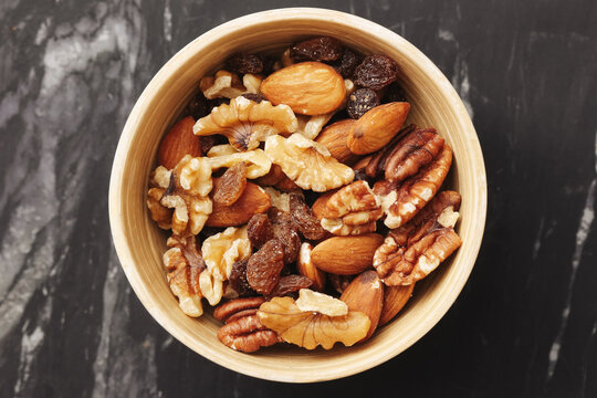 Mixed nuts in wooden bowl. Walnuts almonds pecans and raisins. Natural healthy snack full of energy. Close-up on marble table. Rustic style. Ideal for diet plans and clean eating habits.