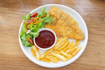 Fish steak with vegetable salad and french fries on a plate, top view