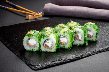 Colorful sushi rolls in green seaweed are beautifully displayed on a slate board