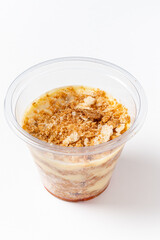 A clear cup holds an enticing layered dessert, featuring creamy textures and a crunchy topping