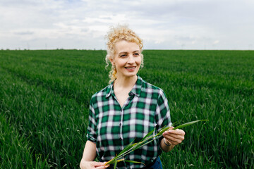 Portrait of adult female farmer standing in green wheat field.