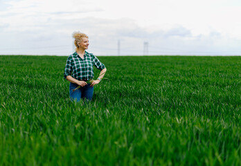 Portrait of adult female farmer standing in green wheat field.