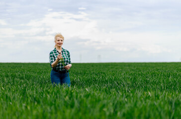 Portrait of adult female farmer standing in green wheat field.