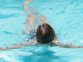 Woman relaxing in outside swimming pool during hot daytime. Back view.