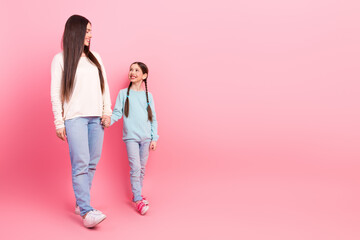Mother and daughter holding hands and enjoying a cheerful moment against a bright pink background