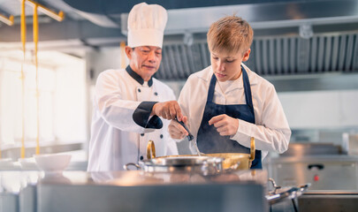 Senior male chef teaches young teenage boys cooking in school kitchen. Education Concept
