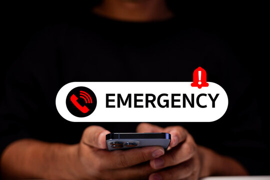 A person holding a smartphone with an emergency alert notification displayed prominently on screen against a dark background.