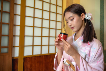 Young attractive Japanese woman in traditional kimono or yukata clothing holding tea in Japanese...