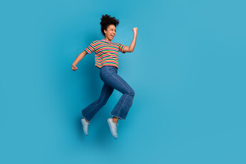 Happy young woman jumping with excitement against blue background expressing positive emotions and vibrant energy