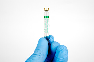 Gloved Hand Holding Medical Vaccine Vial on White Background, Dental Anesthesia Syringe.Close-up of a blue-gloved hand holding a small glass vaccine vial with a green label
