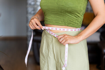 Woman measuring her waist with measuring tape after weight loss