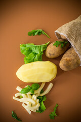 Whole and sliced potatoes on a dark wooden stick on a brown background