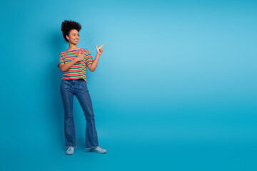 Smiling young woman in a striped shirt pointing with both hands against turquoise background