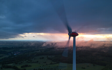 A panoramic view of a wind turbine, illuminated by the last rays of sunlight filtering through the...
