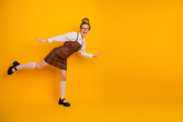 Playful young woman posing in a stylish school uniform against a vibrant yellow background...