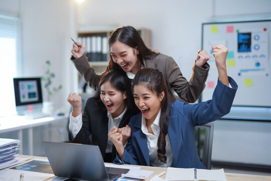 Group of asian businesswomen raising arms and celebrating business achievement looking at laptop in the office