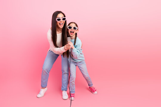 Mother and daughter singing together on pink background showcasing family fun