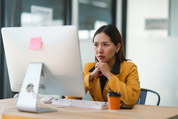 Asian businesswoman with worried expression looking at computer screen while working in modern office