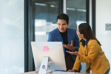 Two business professionals collaborating in an office, discussing strategies while engaging with a desktop computer and sharing ideas