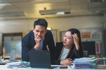 Two Asian businesspeople looking stressed and worried while working late at night in an office, facing challenges and tight deadlines